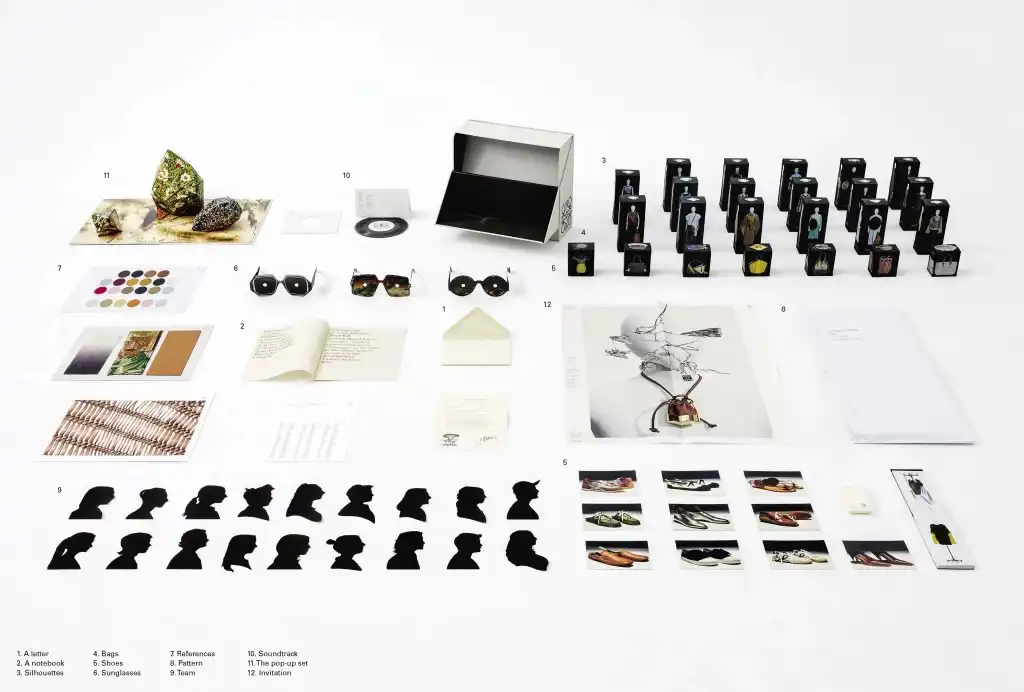 El conjunto completo LOEWE ‘Show in a Box’ Primavera/Verano 2021 dispuesto sobre la mesa, con las siluetas recortadas del equipo de diseño entre las cajas de ropa en miniatura, el disco de vinilo y el escenario pop-up