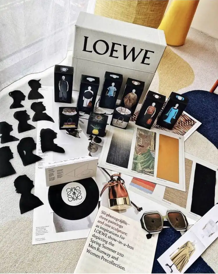 El conjunto de archivo ‘Show in a Box’ de LOEWE dispuesto sobre una alfombra, con las siluetas del equipo, las cajas de ropa en miniatura, el disco de vinilo y las gafas de sol